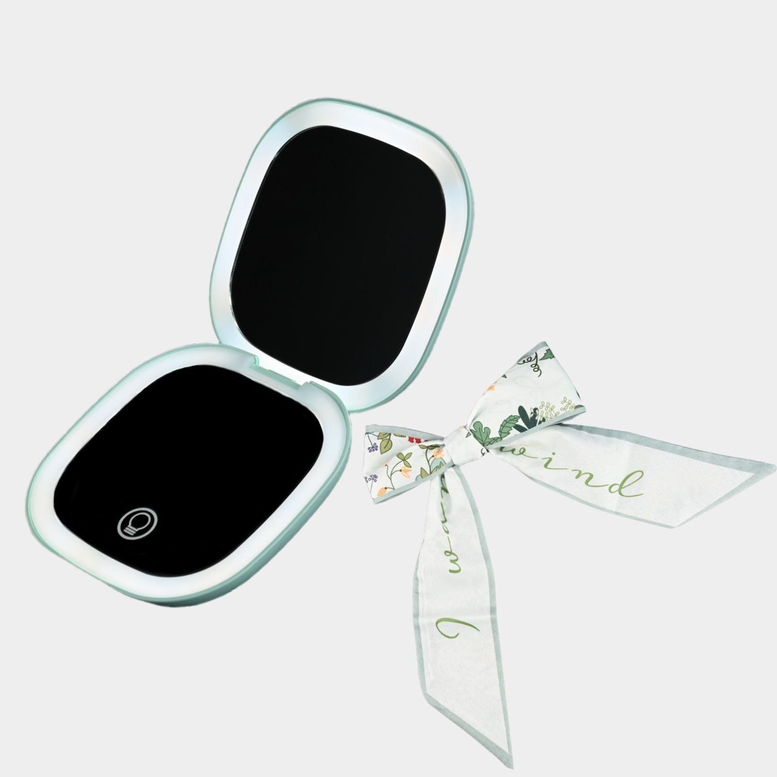 A mint green square compact mirror with a floral-printed ribbon tied to it.